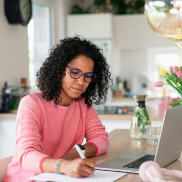 Multiracial woman having home office in kitchen, writing notes.
